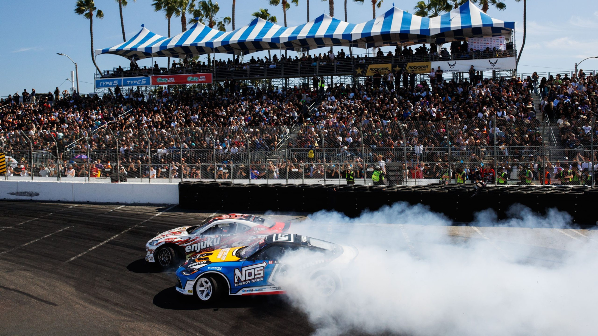 Packed grandstands watching a drift battle with smoke on track